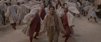 Movie still from “Cyrano” (2021), directed by Joe Wright – A group of men in red and brown costumes; Wide shot, High angle