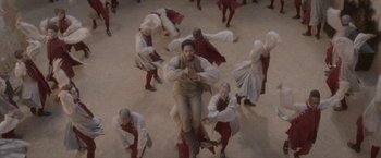 Movie still from “Cyrano” (2021), directed by Joe Wright – A group of men in red and white costumes dancing; Wide shot, Overhead angle