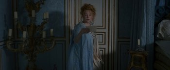 Movie still from “Cyrano” (2021), directed by Joe Wright – A woman standing in front of a wall holding a piece of paper; Medium shot, Over the shoulder angle