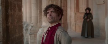 Movie still from “Cyrano” (2021), directed by Joe Wright – A person standing near a building; Medium shot, Low angle