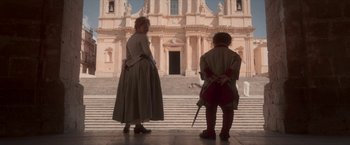 Movie still from “Cyrano” (2021), directed by Joe Wright – A man and a woman standing in front of a building; Wide shot, Low angle