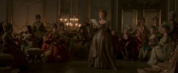 Movie still from “Cyrano” (2021), directed by Joe Wright – A woman in a brown dress is holding a tablet; Wide shot, Low angle