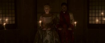 Movie still from “Cyrano” (2021), directed by Joe Wright – A man and a woman standing next to each other holding a candle; Wide shot, Low angle