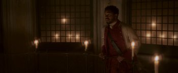 Movie still from “Cyrano” (2021), directed by Joe Wright – A man standing in front of a window with a candle in the background; Medium shot, High angle