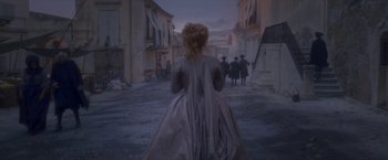 Movie still from “Cyrano” (2021), directed by Joe Wright – A woman in a long dress standing on a street; Wide shot, Over the shoulder angle