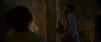 Movie still from “Cyrano” (2021), directed by Joe Wright – A man and a woman standing next to each other in front of a wall; Medium shot, Over the shoulder angle