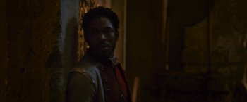 Movie still from “Cyrano” (2021), directed by Joe Wright – A man standing next to a wall in a dark room; Close Up shot, Over the shoulder angle