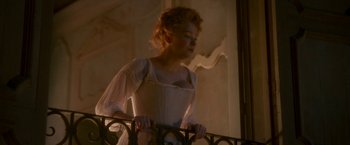 Movie still from “Cyrano” (2021), directed by Joe Wright – A woman in a white dress standing next to a railing; Medium shot, Low angle
