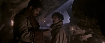 Movie still from “Cyrano” (2021), directed by Joe Wright – A man in a trench coat is holding his hand out to another man in a trench coat; Medium shot, Low angle