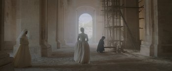 Movie still from “Cyrano” (2021), directed by Joe Wright – A woman in a white dress standing in front of a man in a black robe; Extreme Wide shot, Low angle