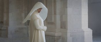 Movie still from “Cyrano” (2021), directed by Joe Wright – A woman dressed in white standing in front of a building; Medium shot, Over the shoulder angle
