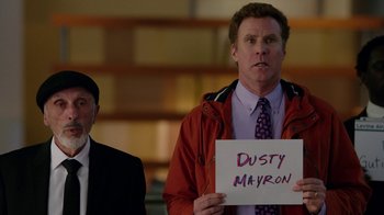 Movie still from “Daddy's Home” (2015), directed by Sean Anders – A man holding up a sign in front of another man in a suit; Medium shot, Low angle