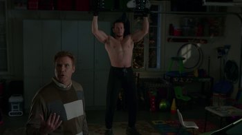 Movie still from “Daddy's Home” (2015), directed by Sean Anders – A man is lifting a barbell in front of another man in a living room; Medium shot, Over the shoulder angle