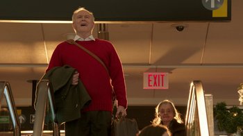 Movie still from “Daddy's Home 2” (2017), directed by Sean Anders – An older man wearing a red sweater while holding a purse; Medium shot, Low angle