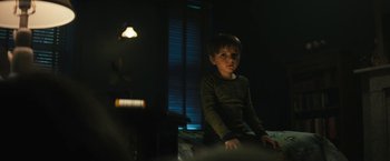 Movie still from “Daniel Isn't Real” (2019), directed by Adam Egypt Mortimer – A young boy sitting on a bed in a dark room at night; Medium shot, Low angle