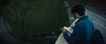 Movie still from “Daniel Isn't Real” (2019), directed by Adam Egypt Mortimer – A person sitting on a park bench reading a book; Medium shot, Low angle