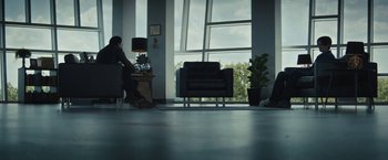 Movie still from “Daniel Isn't Real” (2019), directed by Adam Egypt Mortimer – A man sitting at a table in front of a large window; Wide shot, Low angle