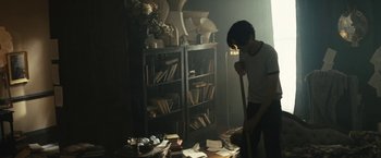 Movie still from “Daniel Isn't Real” (2019), directed by Adam Egypt Mortimer – A person standing in a room with a bunch of books; Medium shot, High angle