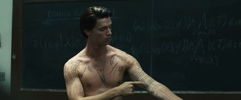 Movie still from “Daniel Isn't Real” (2019), directed by Adam Egypt Mortimer – A shirtless man points to a chalkboard with writing on it; Medium shot, Over the shoulder angle
