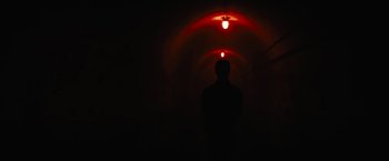Movie still from “Daniel Isn't Real” (2019), directed by Adam Egypt Mortimer – A man standing in a dark room under a light fixture; Wide shot, Low angle