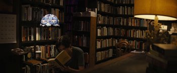 Movie still from “Daniel Isn't Real” (2019), directed by Adam Egypt Mortimer – A man reading a book in front of bookshelves; Medium shot, High angle
