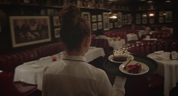 Movie still from “Flower” (2017), directed by Max Winkler – A woman holding a tray with a piece of cake on top of it; Medium shot, Over the shoulder angle