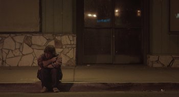 Movie still from “Flower” (2017), directed by Max Winkler – A man sitting on the curb of a street at night; Wide shot, Low angle