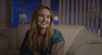 Movie still from “Flower” (2017), directed by Max Winkler – A woman sitting on a couch smiling for the camera; Close Up shot, Over the shoulder angle