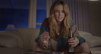 Movie still from “Flower” (2017), directed by Max Winkler – A woman sitting on a couch holding a bottle of beer; Medium shot, Low angle