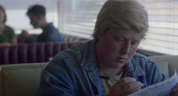Movie still from “Flower” (2017), directed by Max Winkler – A person sitting at a table writing on a piece of paper; Close Up shot, Over the shoulder angle