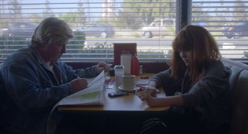 Movie still from “Flower” (2017), directed by Max Winkler – Two people sitting at a table in front of a window; Medium shot, Over the shoulder angle