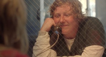 Movie still from “Flower” (2017), directed by Max Winkler – A woman talking on a phone while sitting in front of a fence; Close Up shot, Over the shoulder angle