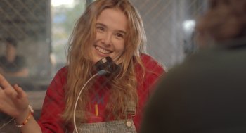 Movie still from “Flower” (2017), directed by Max Winkler – A woman with long hair smiles while holding a microphone; Close Up shot, Over the shoulder angle