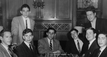 Movie still from “De Palma” (2015), directed by Jake Paltrow – A black and white photo of a group of young men playing chess; Medium shot, High angle