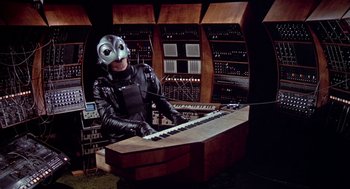 Movie still from “De Palma” (2015), directed by Jake Paltrow – A person wearing a mask playing a keyboard; Medium shot, Low angle