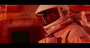 Movie still from “De Palma” (2015), directed by Jake Paltrow – A man in a spacesuit is standing in front of a building; Medium shot, Overhead angle