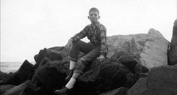 Movie still from “De Palma” (2015), directed by Jake Paltrow – A man sitting on top of a large rock; Medium shot, High angle