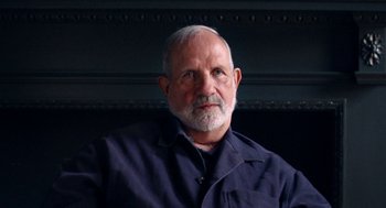 Movie still from “De Palma” (2015), directed by Jake Paltrow – An older man with a gray beard is sitting in front of a wall; Close Up shot, Low angle