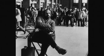 Movie still from “De Palma” (2015), directed by Jake Paltrow – A black and white photo of a man sitting on a chair; Medium shot, Low angle