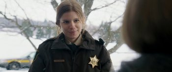 Movie still from “Deadfall” (2012), directed by Stefan Ruzowitzky – A woman wearing a sheriff's badge stands in front of a tree; Close Up shot, Over the shoulder angle