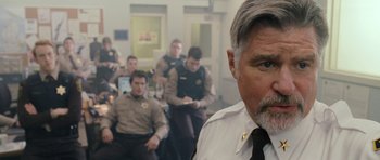 Movie still from “Deadfall” (2012), directed by Stefan Ruzowitzky – A man in a police station with other men in the background; Close Up shot, Over the shoulder angle