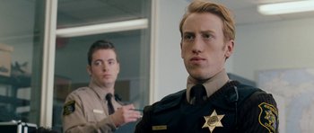 Movie still from “Deadfall” (2012), directed by Stefan Ruzowitzky – A man in a police uniform standing next to another man; Close Up shot, Over the shoulder angle