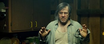 Movie still from “Deadfall” (2012), directed by Stefan Ruzowitzky – A man holding something in his hand while standing in a kitchen; Medium shot, Over the shoulder angle
