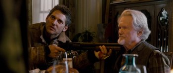 Movie still from “Deadfall” (2012), directed by Stefan Ruzowitzky – Two men sitting at a dinner table with a gun; Medium shot, Over the shoulder angle