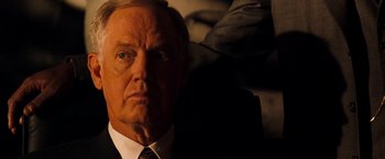 Movie still from “Deep Blue Sea” (1999), directed by Renny Harlin – An older man wearing a suit and tie looking at the camera; Close Up shot, Over the shoulder angle