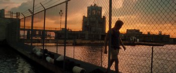 Movie still from “Deep Blue Sea” (1999), directed by Renny Harlin – A person walking on a bridge near a body of water at sunset; Wide shot, Low angle