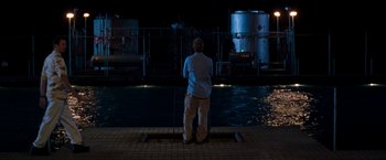 Movie still from “Deep Blue Sea” (1999), directed by Renny Harlin – A man standing in front of a body of water at night; Wide shot, Over the shoulder angle