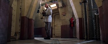 Movie still from “Deep Blue Sea” (1999), directed by Renny Harlin – A man holding a pair of gloves in a room; Wide shot, Low angle