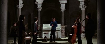 Movie still from “Deep Red” (1975), directed by Dario Argento – A man standing in front of a piano in a room; Wide shot, High angle