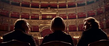 Movie still from “Deep Red” (1975), directed by Dario Argento – A woman sitting in a chair in front of a stage; Medium shot, Over the shoulder angle